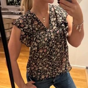 Blommig blus med volangdetaljer - Säljer en söt blommig blus med volangdetaljer från Mango, kommer inte till användning längre. Knytning i ryggen!🥰