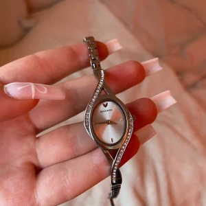 Vintage silverklocka från Sekonda - Fin vintage damklocka från Sekonda med en unik, vriden design. Klockan har en silverfärgad urtavla och ett armband med glittriga stenar. Perfekt för en nice touch till din outfit! Köpt på en marknad i London.