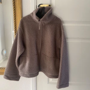Ny brun pilejacka  i storlek M från H&M - Ny med tags.  Färg: brun / mörkbeige Storlek: M Passformen är i en normal avslappnad form.  Ej oversize. Vill du ha plats för tjocktröja under så gå gärna upp en storlek. Märke: HM Pile Teddy 