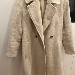 Beige kappa med bälte - Elegant beige kappa med knappar och bälte i midjan. Är i bra skick. 