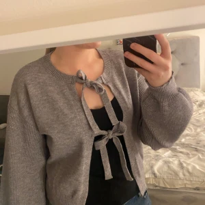 Grå kofta - Säljer en mysig grå kofta med knytband framtill. Koftan har långa ärmar och en ribbad kant vid ärmslut och nederkant. Perfekt för lager-på-lager-stil. Aldrig använt. Vet ej vart den är från. 