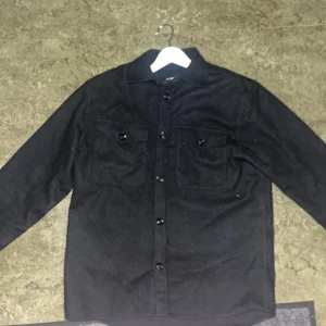 Marinblå overshirt från j.lindeberg - Snygg marinblå filtovershirt med knappar från j.lindeberg. Perfekt för både vardag och mer avslappnade tillfällen. Nypris cirka 3000kr. Passar 170-180 skulle jag säga.
