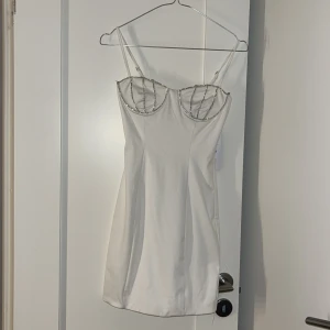 Vit klänning med strassdetaljer - Snygg vit kortklänning med smala axelband och strassdetaljer. Den är köpt i Spanien. Aldrig använd då jag upptäckte att den var för liten när jag kom hem. Perfekt till nyår🥂