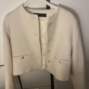 Vit kofta från Zara - Säljer en stilren vit kavaj från Zara med rund hals och knappar framtill. Kavajen har en elegant struktur och två fickor med knappdetaljer. Perfekt för en chic look. Har inte använts någon gång och säljer för att jag vill ha en större storlek.💕💕