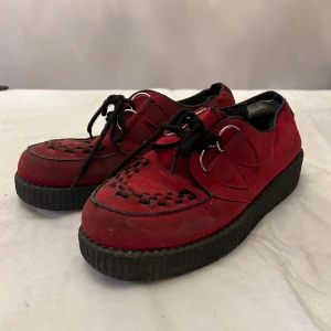 Röda creeper mockaskor med snörning - Snygga röda mockaskor med svart snörning och dekorativa detaljer på ovansidan. Skorna har en robust svart sula som ger en cool kontrast till det röda mockamaterialet.