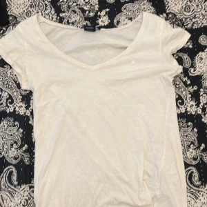 Vit t-shirt från Ralph Lauren Sport - Säljer en klassisk vit t-shirt från Ralph Lauren Sport i 100% bomull. T-shirten har en v-ringad hals och korta ärmar med en diskret broderad logga på bröstet. Perfekt för en stilren och avslappnad look.