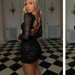 Svart glittrig klänning - Snygg svart glittrig klänning med långärmad design och öppen rygg. Klänningen har snörning i ryggen och är perfekt för en festlig kväll.