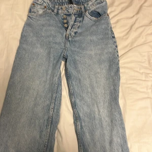 Blå jeans med knappar - Säljer ett par ljusblå jeans med hög midja och knappar framtill. De har en loose passform och raka ben. Perfekta för en avslappnad stil.