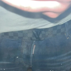 Svart bälte från Louis Vuitton - Snyggt svart bälte från Louis Vuitton med klassiskt rutigt mönster och ett stilrent LV-spänne. Perfekt för att ge din outfit en lyxig touch.