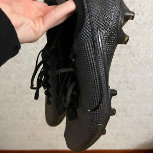 Nike mercurial vapor 13 - Säljer ett par svarta fotbollsskor med snörning och dobbar för bra grepp på planen. Skorna har en stilren design med en texturerad yta för bättre bollkontroll. Aningen slitage fram på tån 