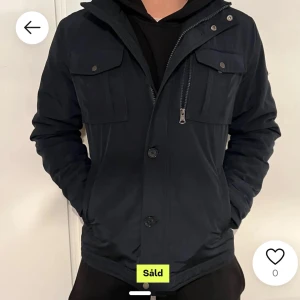 Fieldjacka från J Lindberg  - Snygg blå jacka med dragkedja och knappar framtill. Jackan har två bröstfickor med lock och knappar. Perfekt för vår och höst. Grymt skick och sällan använd. Köpte på plick i höstas men knappt använt. Skriv för fler bilder. Modellen är bailey.