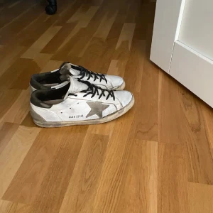 Vita sneakers från Golden Goose - Snygga vita sneakers med en grå stjärna på sidan och svarta snören. Perfekta för en avslappnad stil. Passar även mindre storlekar.