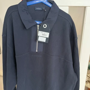 Marinblå tröja med dragkedja från Redgreen - Snygg marinblå tröja från Redgreen med dragkedja och krage. Perfekt för en stilren look. Tröjan har långa ärmar och en diskret logga på bröstet.