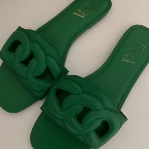 Gröna sandaler från Zara - Säljer dessa snygga gröna sandaler/tofflor från Zara med flätad detalj på ovansidan. Perfekta för sommarens varma dagar. Enkla att matcha med olika outfits. Endast använd ett par få gånger och är därav i väl drift bra skick!🩷