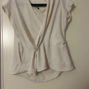 Vit omlottblus - Säljer en stilren vit omlottblus med korta ärmar och knytning framtill. Perfekt för en elegant och avslappnad look. Från zara i storlek L