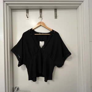 Svart blus med spetsdetaljer - Snygg svart blus med v-ringning och spetsdetaljer längs kanterna. Perfekt för en stilren look. Helt oanvänd Zara topp/blus. Säljer då jag köpte två i olika storlekar och valde den andra. Endast provad. Normal i storleken.  Jättefin topp, den jag har i rätt storlek har använts flitigt🤩