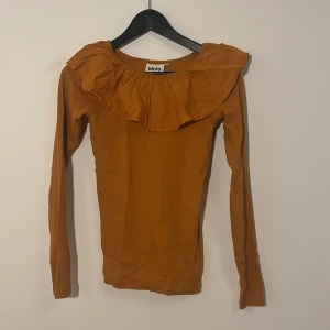 Brun långärmad topp från Molo - Säljer en snygg senapsgul långärmad topp från Molo med volangdetalj runt halsen. Perfekt för höst och vår. Toppen är i en mjuk och bekväm bomullskvalitet.