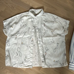 Vit kortärmad skjorta från Levi's - Säljer en vit kortärmad skjorta från Levi's i storlek S. Skjortan har ett unikt abstrakt mönster i svart, gult och rosa. Den är gjord av bomull och har knappar framtill. Perfekt för sommaren eller en avslappnad fest!