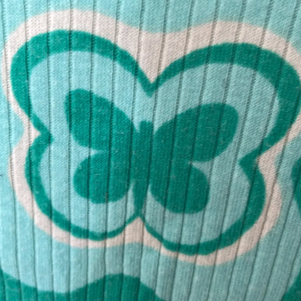 Säljer en superfin topp från H&M i storlek XS. Den är grön och vit med ett coolt, vågigt mönster och en stor fjäril i mitten. Toppen är ribbad och har korta ärmar. Perfekt för sommaren och vårens alla äventyr! 🌸. Yläosat.