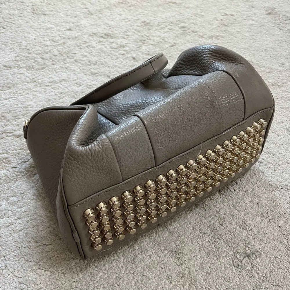 Säljer min Alexander Wang Rockie bag i grått skinn med guldfärgade nitar på undersidan. Väskan har två handtag och en dragkedja för att stänga den. Perfekt för både vardag och fest! ✨Använd men i fint skick!. Laukut & Käsilaukut.