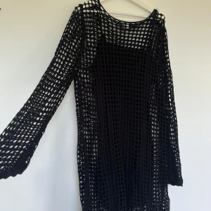 Svart stickad klänning - Säljer en svart stickad klänning med ett coolt nätmönster. Klänningen är långärmad och har en lös passform. Perfekt för en sommarfest eller en dag på stranden. Den är i nyskick och väldigt bekväm att ha på sig. inbyggd underklänning