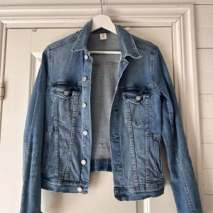 Blå jeansjacka från H&M - Säljer en snygg blå jeansjacka från H&M i storlek S. Jackan har en klassisk design med två bröstfickor med knappar och två sidofickor. Den är tillverkad i denim och har en normal passform. Perfekt för vår och höst! 🧥💙