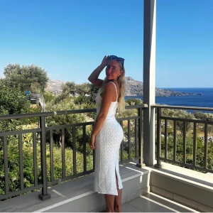 Vit långklänning med spetsdetaljer - Säljer en superfin vit långklänning med spetsdetaljer. Klänningen är ärmlös och har en tight passform som framhäver figuren. Perfekt för sommarens alla fester eller en dag på stan. Den har en liten slits där bak som gör den extra snygg och bekväm att röra sig i. 