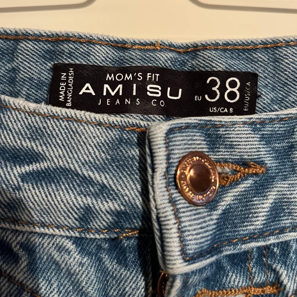 Säljer ett par snygga blå mom jeans från Amisu i storlek 38. De har en cool sliten look med flera revor på både fram- och baksidan. Perfekta för en avslappnad och trendig stil. De är högmidjade och har en knapp och dragkedja framtill. Passar perfekt till vardags eller en chill utekväll. 🥰. Jeans & Byxor.