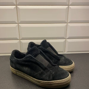 Axel arigatos skor - Svarta arigatos tyg laceless skor. Billigare vid snabb affär. Riktigt sköna och stiliga. Till mesta dels skitiga men lite skador finns nån söm är öppen mm.  Vid fågor skicka meddelande, svarar så fort jag kan.