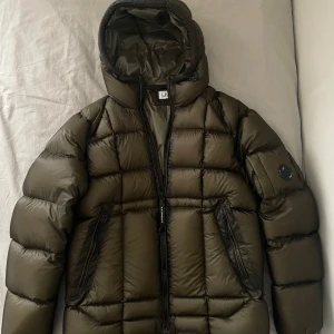 Svart dunjacka från C.P. Company - Grön dunjacka från CP Company. Köptes på Ekbergs och kvitto + taggar finns. Nypris är 6899kr. Jackan köptes i februari och har knappt använts. Jackan är i nyskick förutom ett millimeterstort hål längst ner på högra ärmen. Skriv gärna vid frågor. 