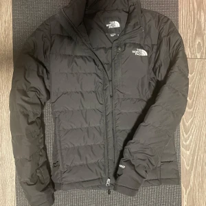 Svart dunjacka från The North Face - Säljer en svart dunjacka från The North Face i storlek herr XS. Jackan är perfekt för kyliga dagar med sin quiltade design och dragkedja framtill. Den har långa ärmar och är superbekväm att ha på sig. Passar perfekt för både vardag och utomhusaktiviteter!