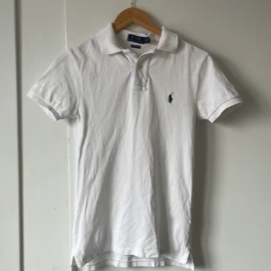 Vit pikétröja från Ralph Lauren - Säljer en klassisk vit pikétröja från Ralph Lauren i storlek XS. Tröjan är i slim fit och har korta ärmar. Perfekt för en stilren och avslappnad look. Den har den ikoniska loggan broderad på bröstet. Passar både till vardags och lite finare tillfällen.