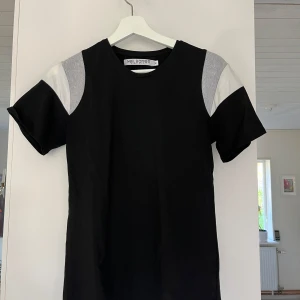 Svart och vit t-shirt från Neil Barrett - Säljer en snygg svart t-shirt från Neil Barrett med vita och grå detaljer på ärmarna. Den är gjord av 100% bomull vilket gör den superbekväm att ha på sig. Perfekt för både vardag och fest!