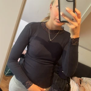 Svart långärmad topp med spetsdetaljer - Säljer en snygg svart långärmad topp med fina spetsdetaljer vid halsen och ärmsluten. Toppen är ribbad och har en tight passform, perfekt för både vardag och fest. Den är i bra skick och superbekväm att ha på sig!