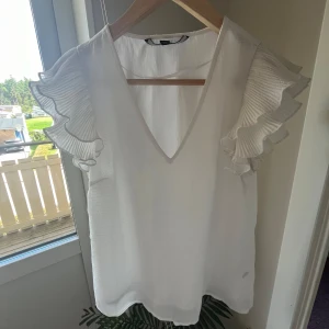 Vit blus från Vero Moda - Säljer en superfin vit blus från Vero Moda i storlek XS. Den har en v-ringad design och korta ärmar. Perfekt för både vardag och fest! Använd en gång.