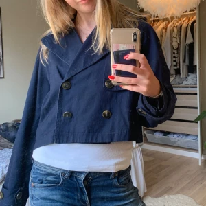 Mörkblå croppad jacka - Säljer en snygg mörkblå croppad jacka med dubbelknäppning. Jackan har en cool oversized passform och stora knappar framtill. Perfekt för vår och höst när du vill ha en stilren look.