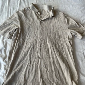 Beige pikétröja från H&M - Säljer en beige pikétröja från H&M i storlek M. Tröjan är i bomull och har korta ärmar. Den har en klassisk pikékrage med knappar. Perfekt för en avslappnad och stilren look. Tröjan är i välanvänt skick men fortfarande i bra form. Passar bra till både vardag och finare tillfällen. Frågor? Skriv!