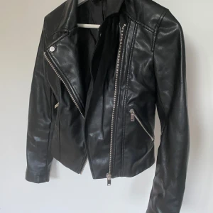 Svart skinnjacka från H&M - Säljer en snygg svart skinnjacka från H&M i storlek 34. Jackan har en cool bikerstil med dragkedja framtill och två snedställda fickor med dragkedjor. Perfekt för höst och vår, och den ger en edgy touch till vilken outfit som helst. Jackan är i bra skick och redo för nya äventyr!