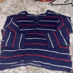 Randig stickad tröja från Gina Tricot - Säljer en superfin stickad tröja från Gina Tricot i storlek M. Den är mörkblå med röda och vita ränder och har en söt knytning vid halsen. Perfekt för höst och vinter när man vill vara både varm och stilren. Tröjan är i bra skick och redo för en ny ägare!