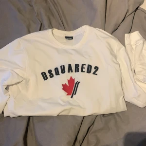 Dsquared2 tröja - Säljer en stilren vit långärmad tröja från Dsquared2 deras logga på framsidan. Tröjan har ribbade muddar vid ärmslut och nederkant. Perfekt för en avslappnad look.