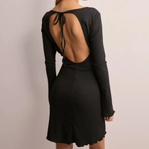 Svart klänning med öppen rygg - Snygg svart klänning med öppen rygg och knytband. Långärmad design med fina knytningar vid ärmsluten. Använd 2 gånger
