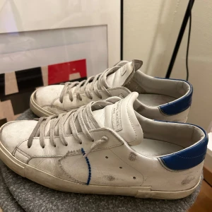 Vita sneakers från Philippe Model - Snygga vita sneakers från Philippe Model med blå detaljer på hälen. Skorna har en klassisk design med snörning och en bekväm passform. Perfekta för en stilren look.