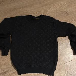 Svart tröja från Louis Vuitton - Säljer en stilren svart tröja från Louis Vuitton med deras ikoniska monogrammönster. Tröjan har långa ärmar och en rund halsringning. Perfekt för en trendig look.