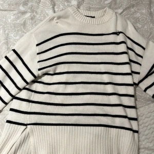 Vit och svart randig tröja från 157 - Säljer en stilren vit tröja med svarta ränder från 157. Tröjan har en rund hals och långa ärmar, perfekt för en avslappnad look. Den är ribbad vid ärmslut och nederkant vilket ger en snygg detalj. Passar bra till både jeans och kjol. Den har ett litet hål längst upp vid halsen som jag har sytt ihop.