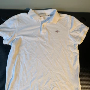 GANT grisch T-shirt - Säljer en klassisk vit pikétröja från GANT i regular fit. Tröjan har korta ärmar och en broderad logotyp på bröstet. Perfekt för en stilren och avslappnad look. Jätte bra skick och är som ny. Storlek S