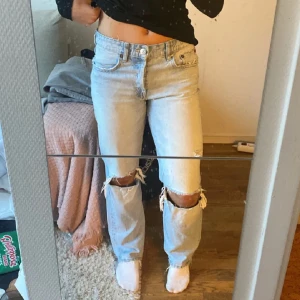 Ljusblå jeans med slitningar från Zara - Säljer ett par ljusblå jeans från Zara med slitningar på knäna. De har en låg midja och en straight passform. Perfekta för en avslappnad stil.
