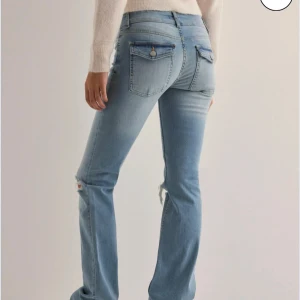 Ljusblå bootcut jeans - Snygga ljusblå jeans med bootcut-stil och slitna detaljer på knäna. De har en låg midja och klassiska femficksdesign med knappar.