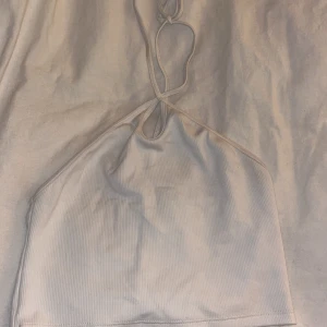 Vit ribbad halterneck topp från Zara - Säljer en stilren vit ribbad halterneck topp från Zara. Toppen har en enkel design med smala band som knyts i nacken. Perfekt för varma dagar eller som en del av en lager-på-lager look.