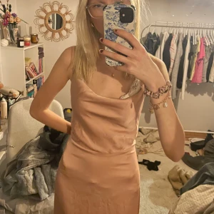 Ljusrosa långklänning med öppen rygg - Elegant ljusrosa långklänning i satin med smala axelband och en vacker öppen rygg. Klänningen har en mjuk och följsam passform som ger en stilren look. Perfekt för speciella tillfällen. jag är 170cm