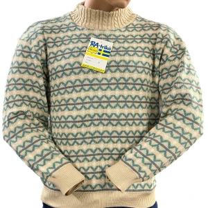 Beige och blå mönstrad stickad tröja från RA-trikå - Säljer en mysig beige stickad tröja från RA-trikå med blått geometriskt mönster. Tröjan har en hög ribbad krage och långa ärmar med ribbade muddar. Perfekt för kyliga dagar! Finns i M, L och XL